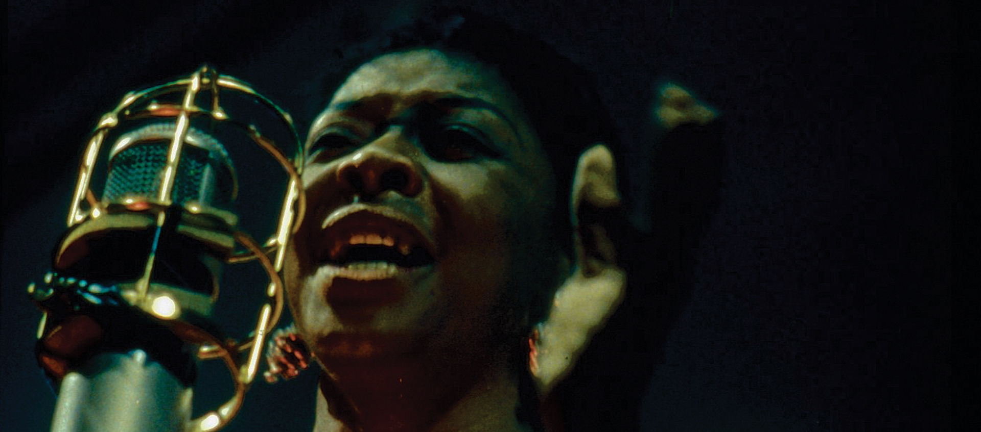 Dinah Washington, seen from neck up, sings into a large bullet microphone in a scene from the documentary Jazz on a Summer's Day