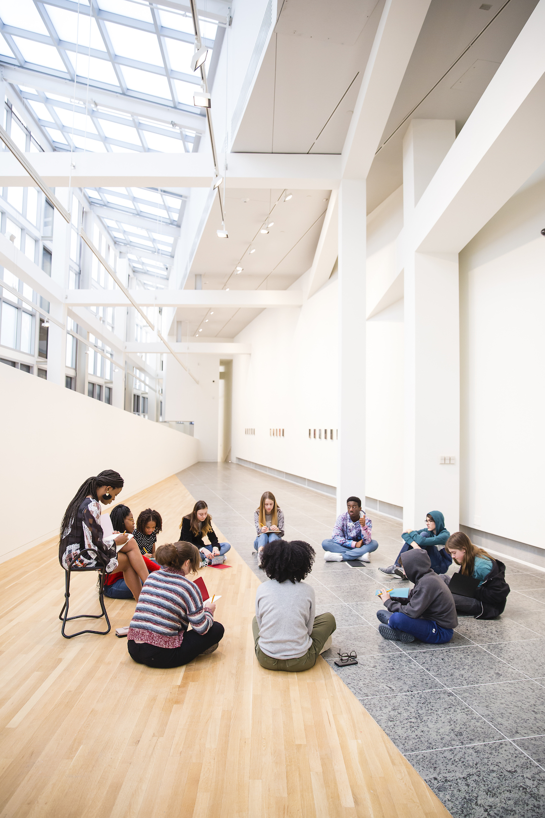 A group of 11 high school students and educators sit in a circle in a gallery at the Wexner Center for the Arts
