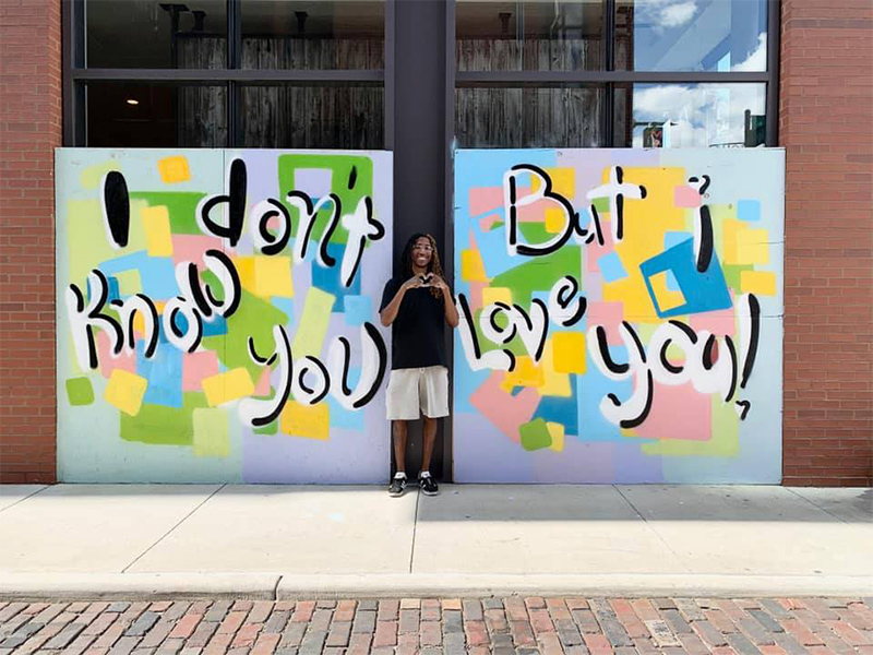 Columbus artist Hakim Callwood stands in front of a mural he's created for a boarded up storefront that reads, "I don't know you but I love you"
