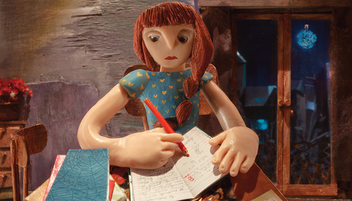 A woman, constructed from clay, sits at a desk and writes in a journal.